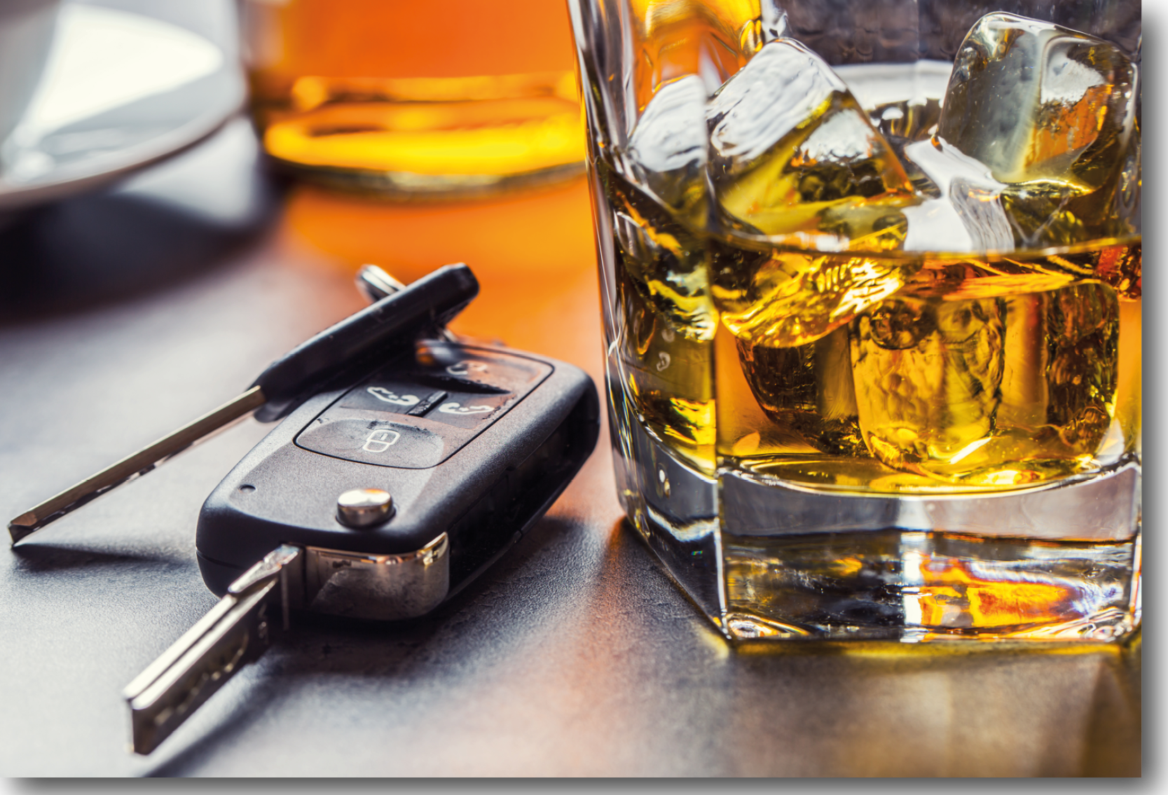 A set of car keys placed on a table next to a alcoholic drink