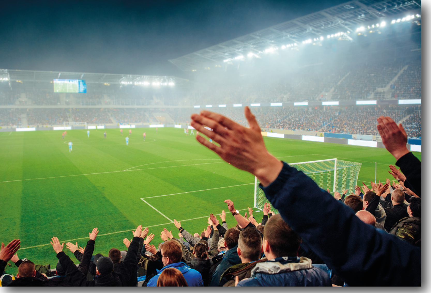 Football fans standing up and singing inside a football stadium with a game ongoing